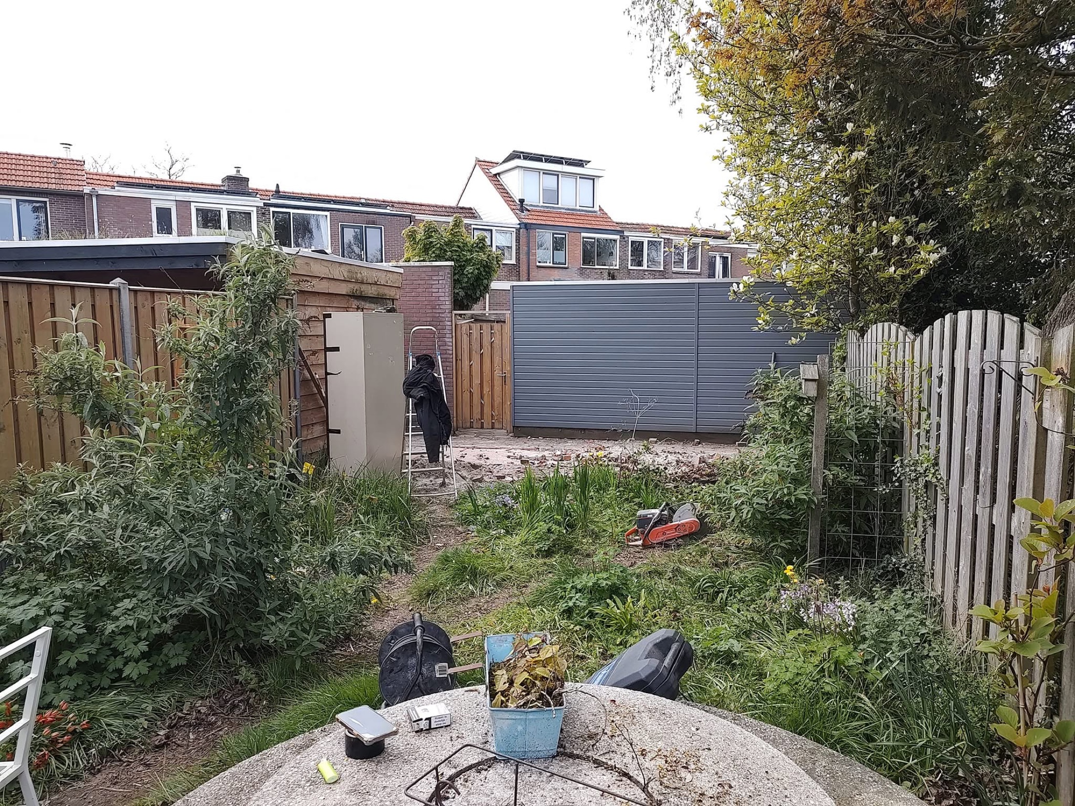 Voor de tuinrenovatie: verouderde tuin met veel begroeiing en losse materialen