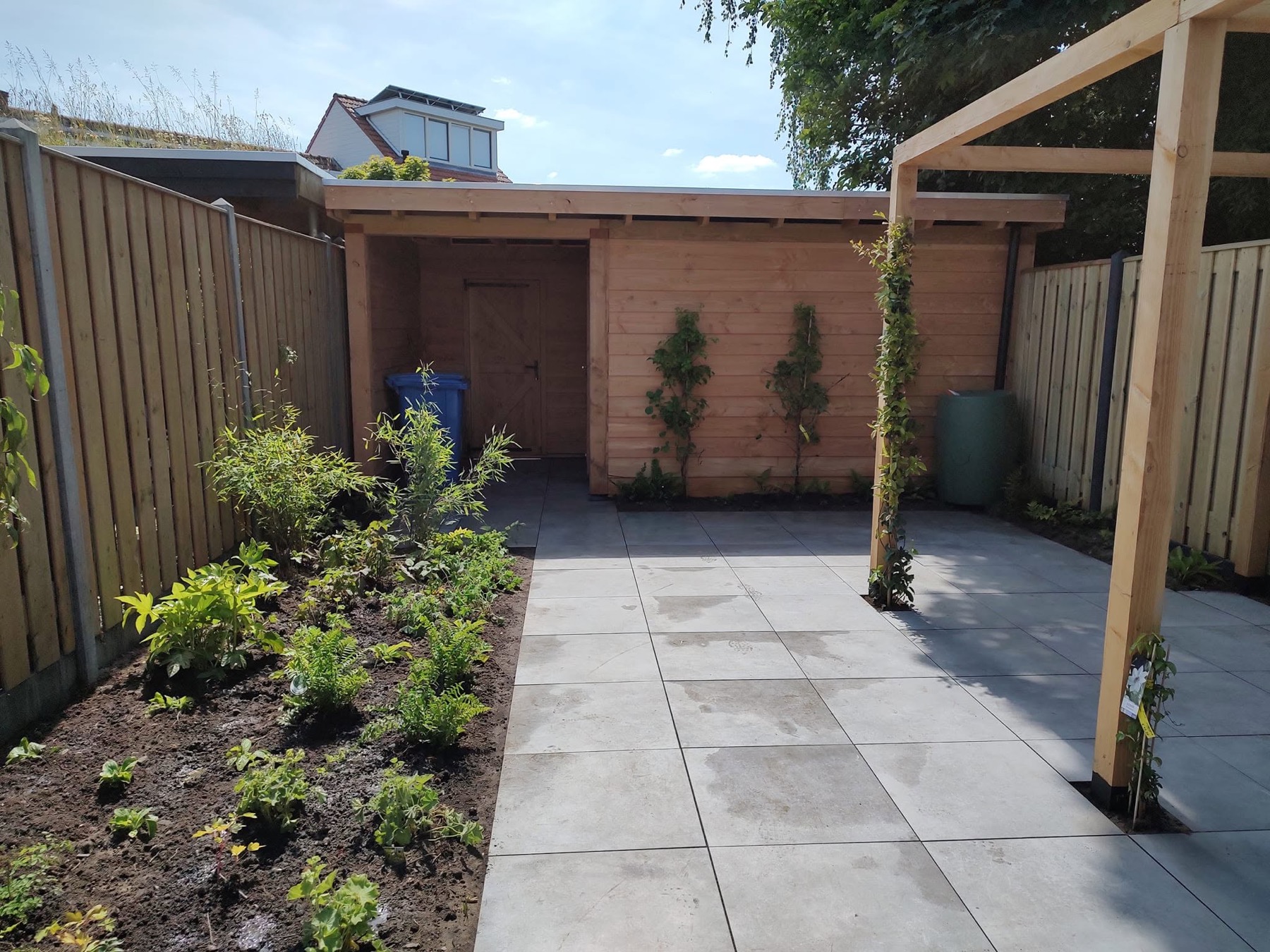 Tuin met houten berging, pergola, bestrating en nieuwe beplanting