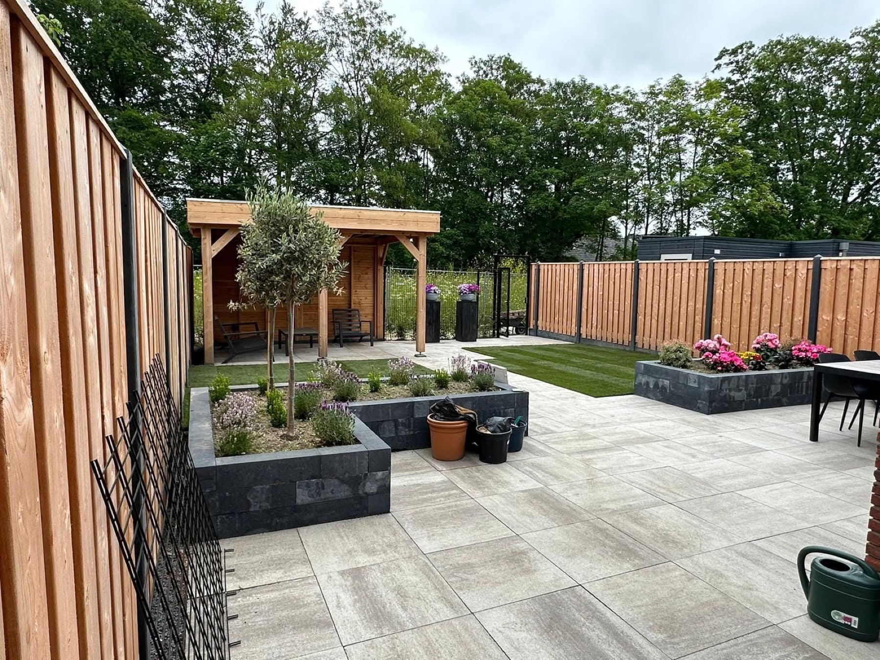 Moderne stadstuin met groot terras, verhoogde borders, gazon en houten overkapping